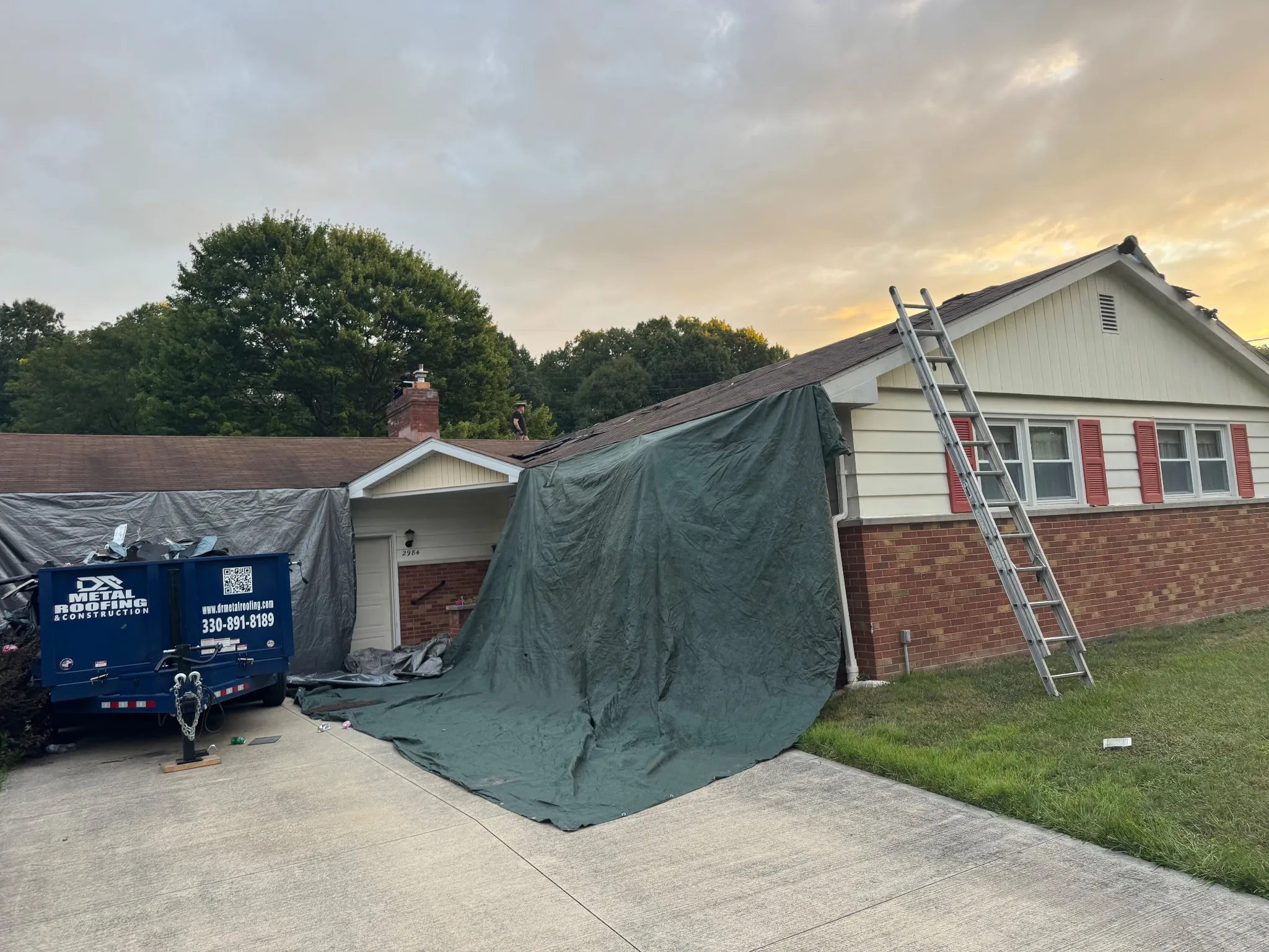 DR crew mid tear-off with the branded dump trailer on site